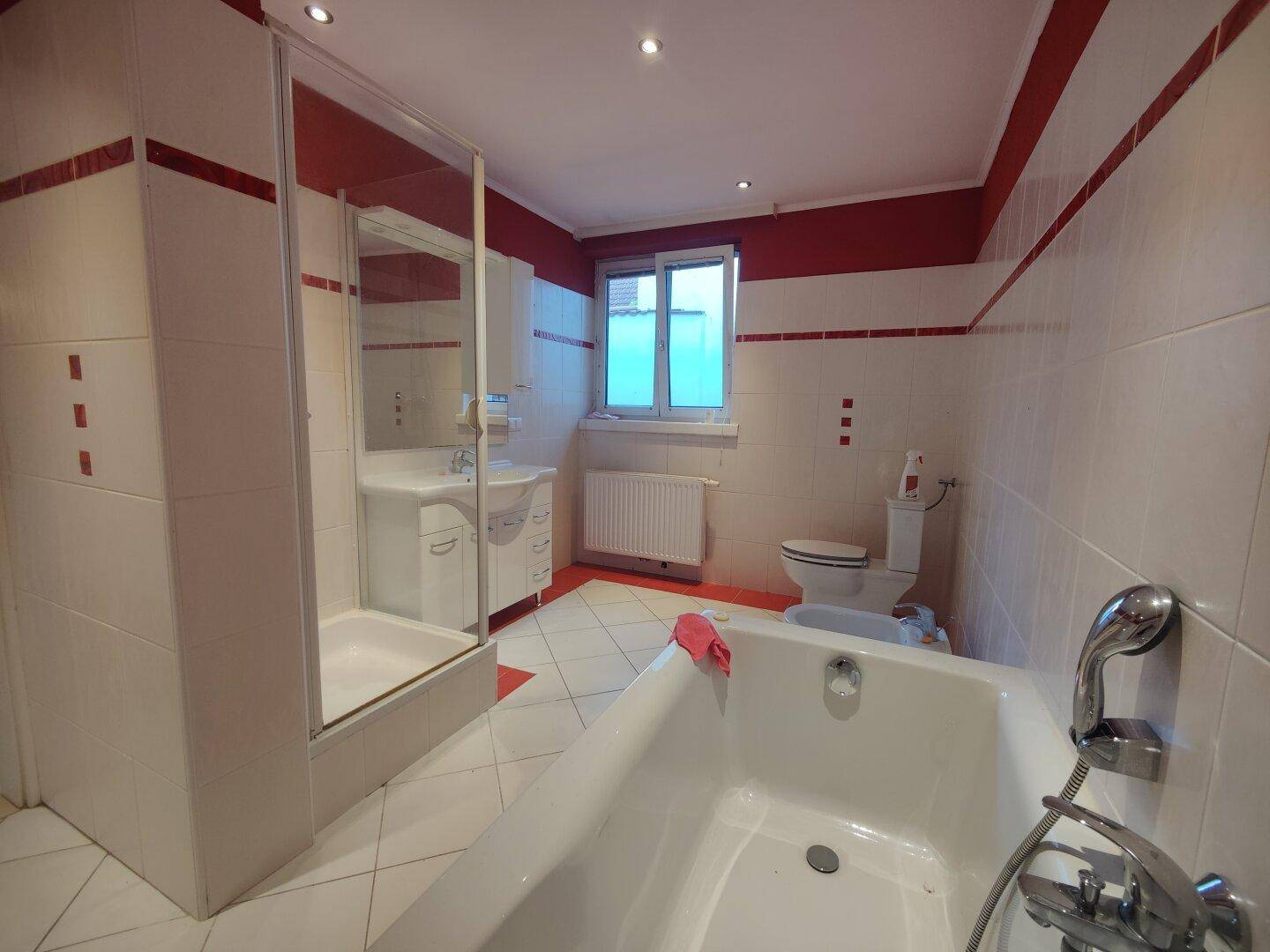 Geräumiges Badezimmer mit Badewanne, Duschkabine, WC und markanten rot-weißen Fliesen.