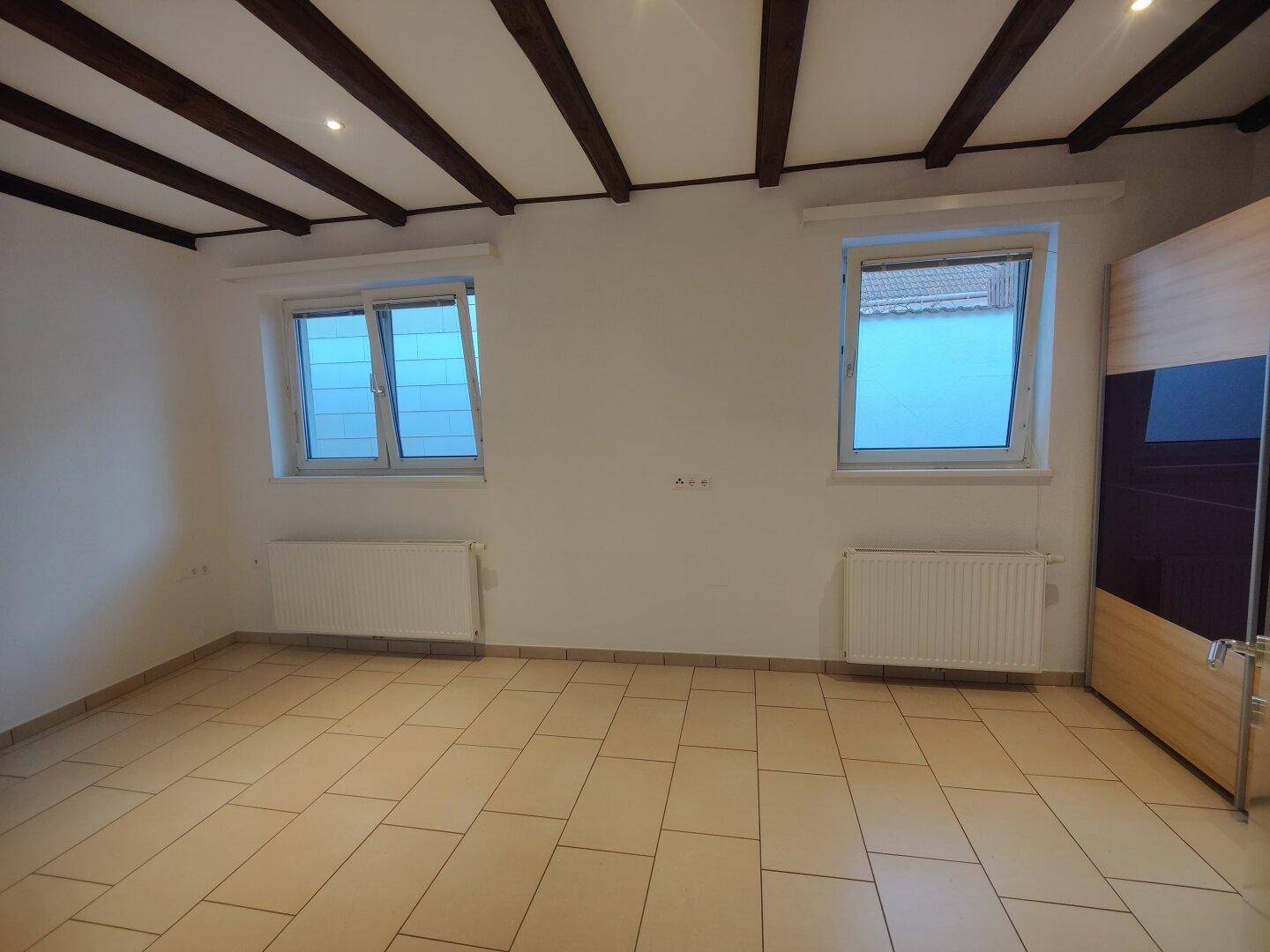 Helles Schlafzimmer mit Fliesenboden, zwei Fenstern und Heizkörpern.