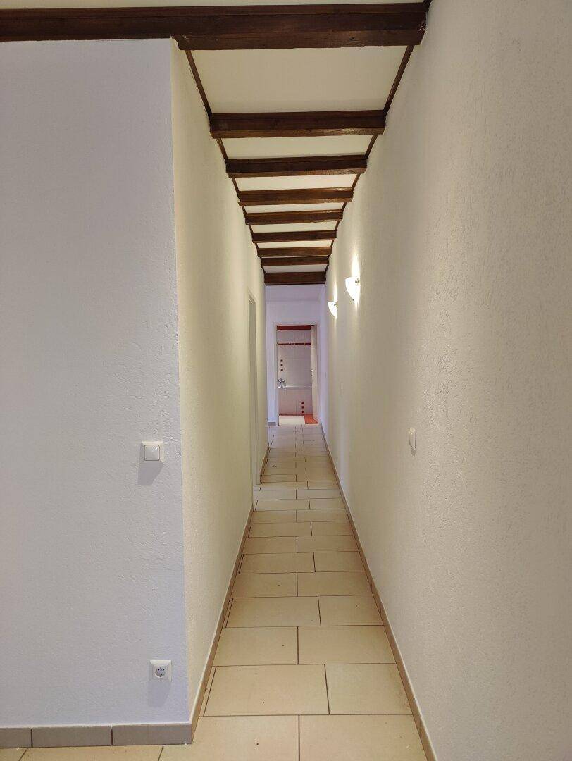 Langer, schmaler Flur mit hellen Fliesen und sichtbaren Holzbalken an der Decke.