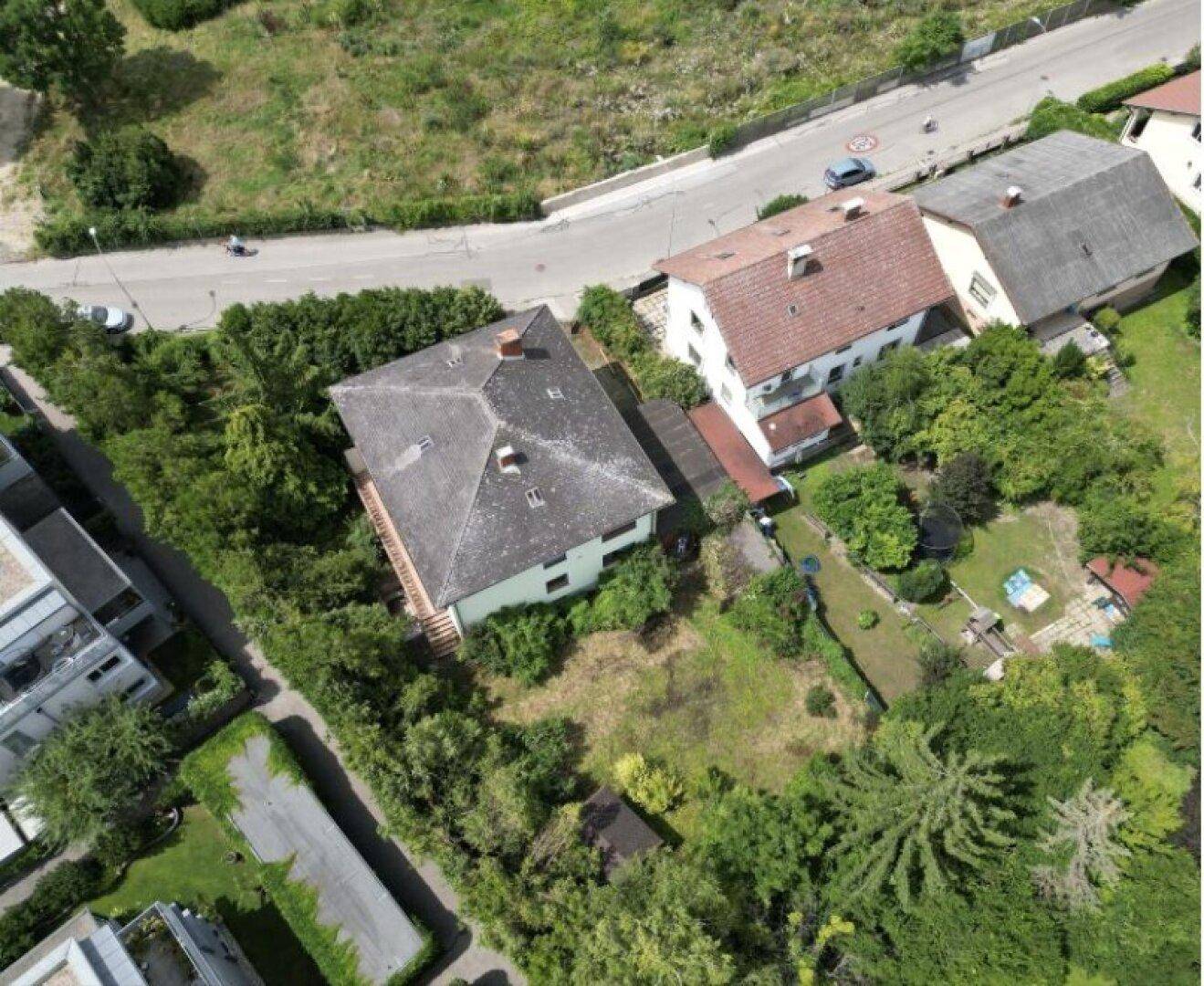 Luftaufnahme eines Einfamilienhauses mit großem Garten, umgeben von Bäumen und einer Straße.