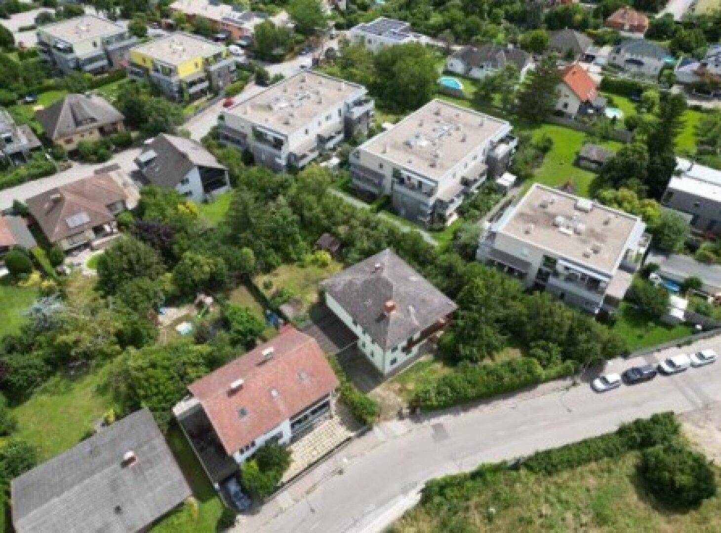 Weitläufige Luftaufnahme einer Wohnsiedlung mit verschiedenen Haustypen und viel Grünfläche.