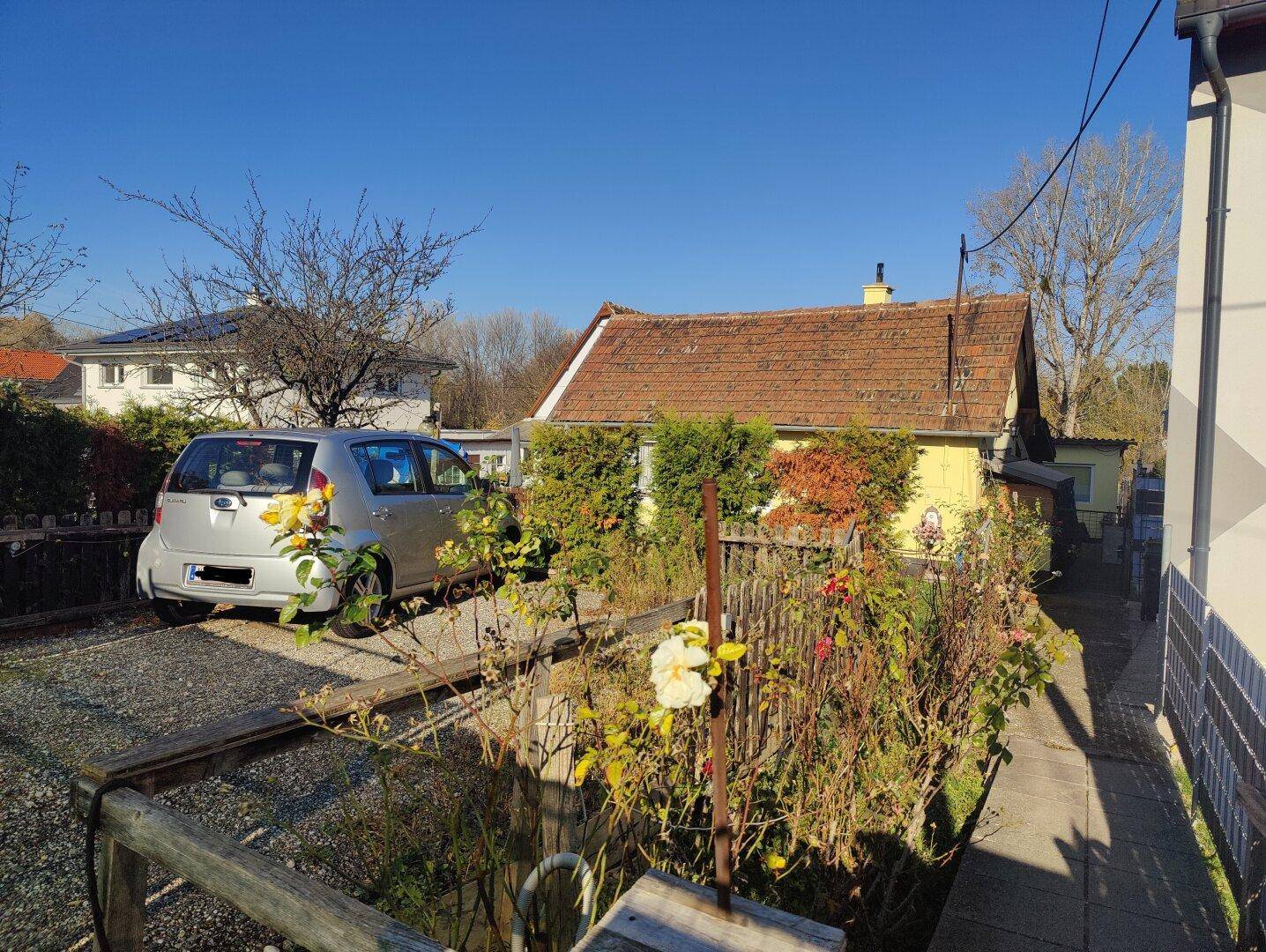 Sonnenbeschienene Außenansicht des Hauses mit gepflegter Auffahrt und angrenzendem Gebäude.