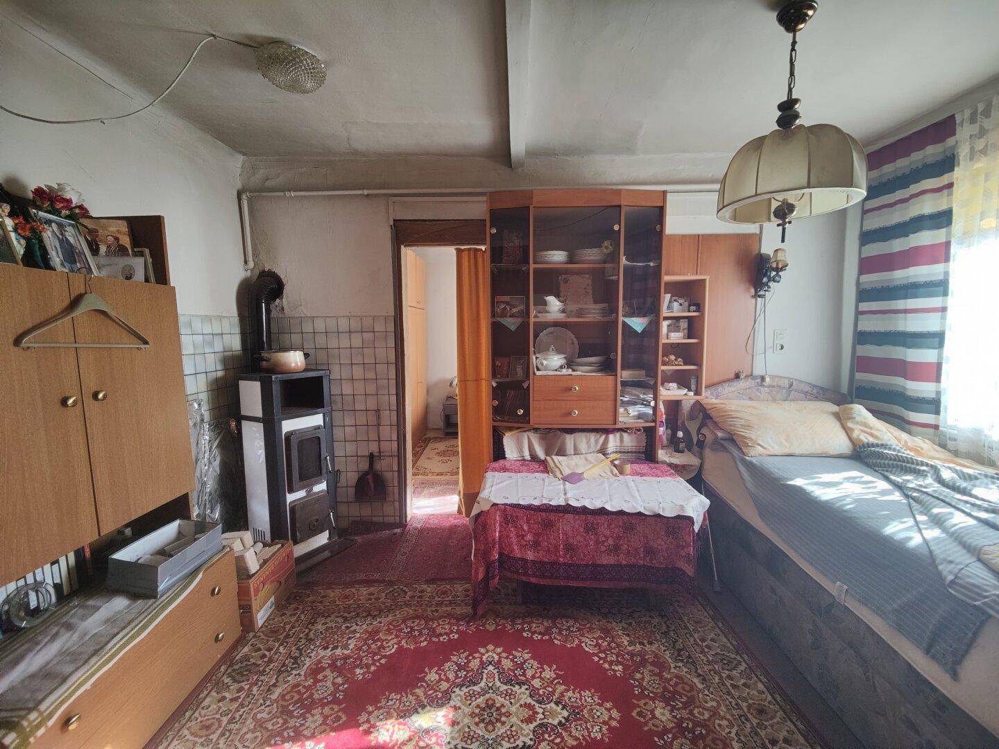 Gemütlicher Innenraum mit Bett, Schrank, Holzofen und traditionellem Teppich, der eine warme Atmosphäre schafft.