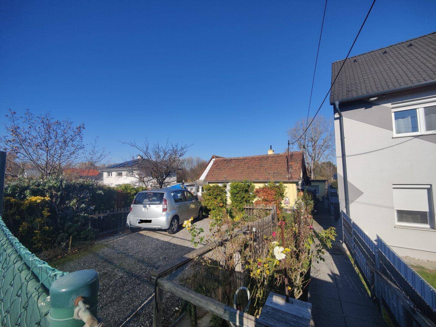 Außenansicht eines kleinen gelben Hauses mit Kiesauffahrt und parkendem Auto an einem sonnigen Tag.