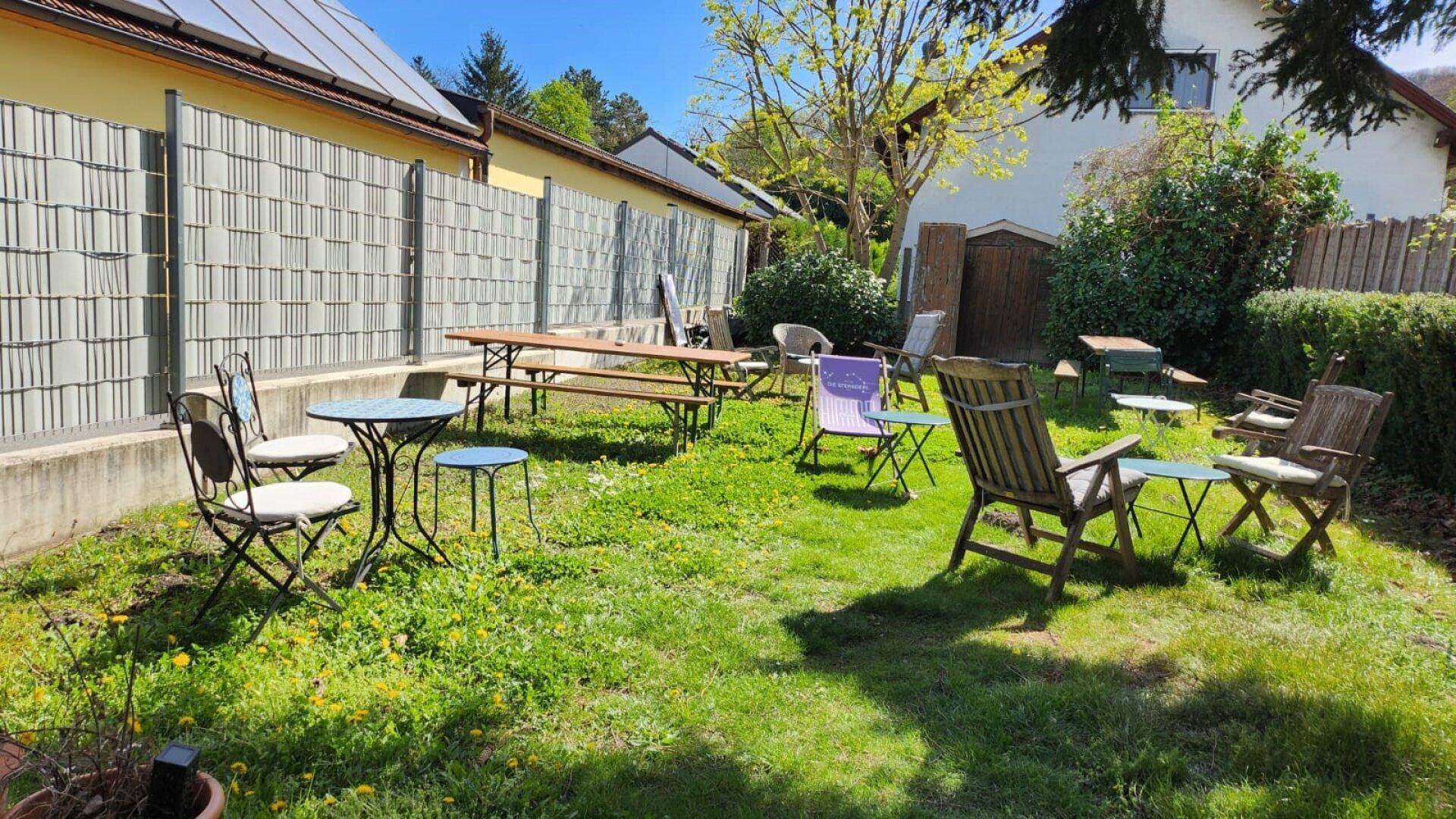 Großer, grüner Gartenbereich mit verschiedenen Sitzgelegenheiten und einem Zaun im Hintergrund.