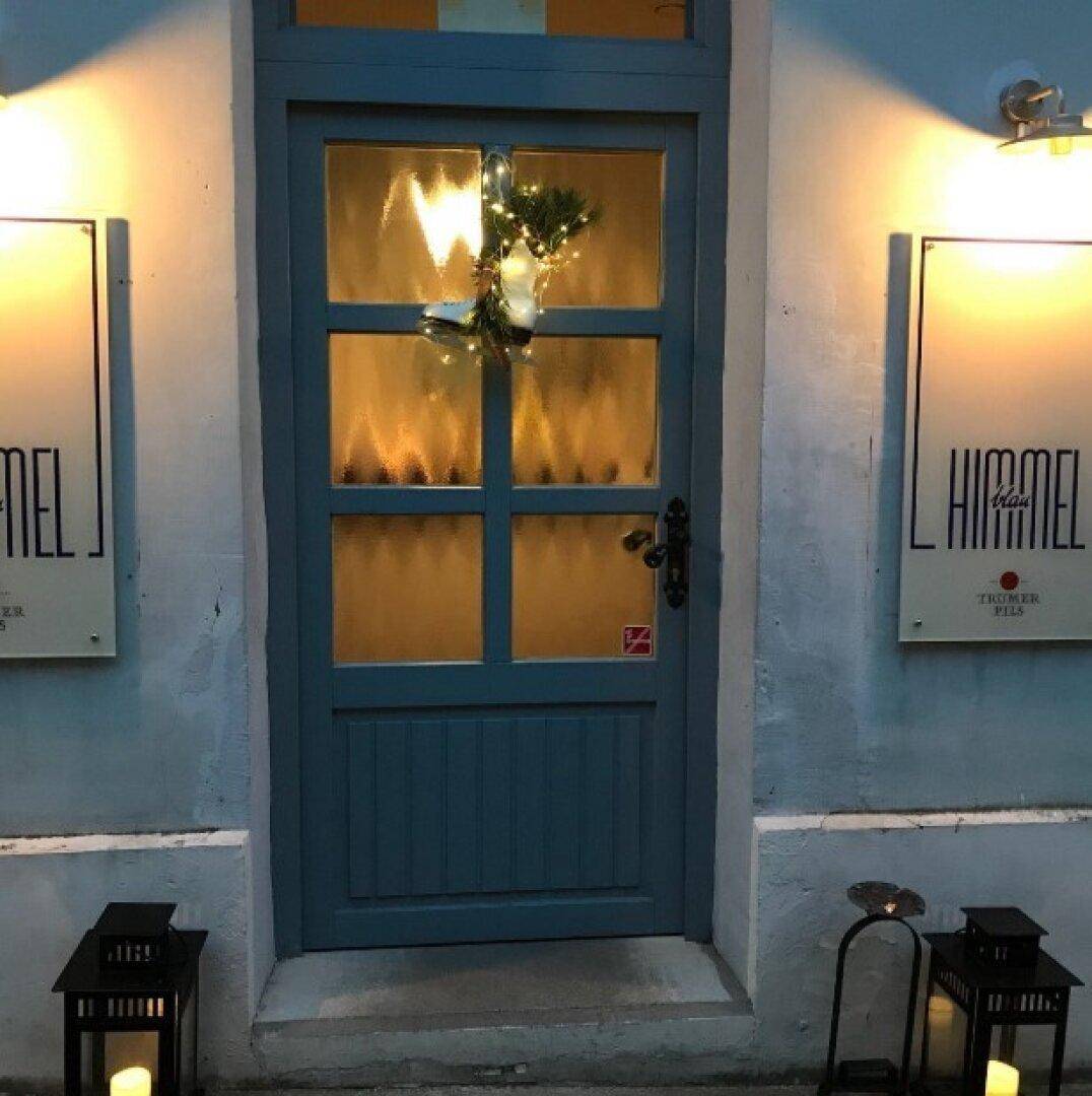 Eingangstür in Blau mit Glasfeldern und festlicher Dekoration, beleuchtet in der Nacht.
