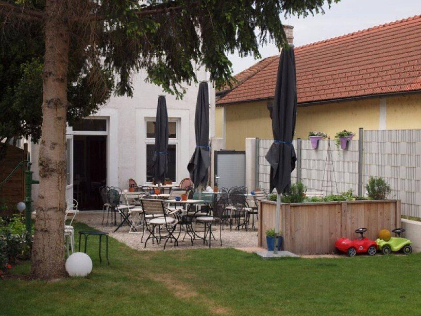 Gepflegter Gastgarten mit Sitzgelegenheiten, Hochbeet und Spielzeugautos für Kinder.