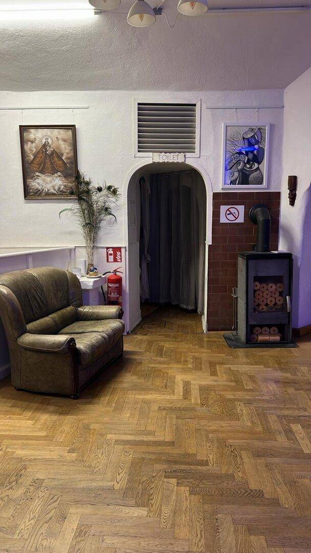 Gemütlicher Loungebereich mit Ledersofa, Kaminofen und Holzboden, der zu einem Toilettenbereich führt.
