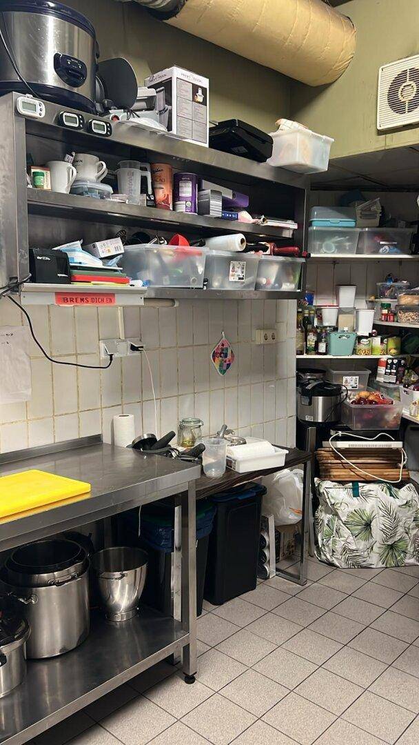 Lagerbereich einer Gewerbeküche mit Regalen voller Vorräte und Utensilien, gut organisiert und funktional.