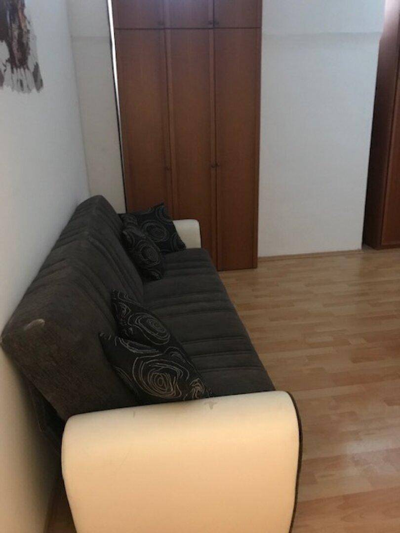 Wohnzimmer mit dunklem Sofa, Holzschrank und hellem Laminatboden.