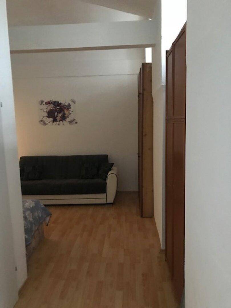 Wohnbereich mit dunklem Sofa, Holzschränken und hellem Laminatboden.
