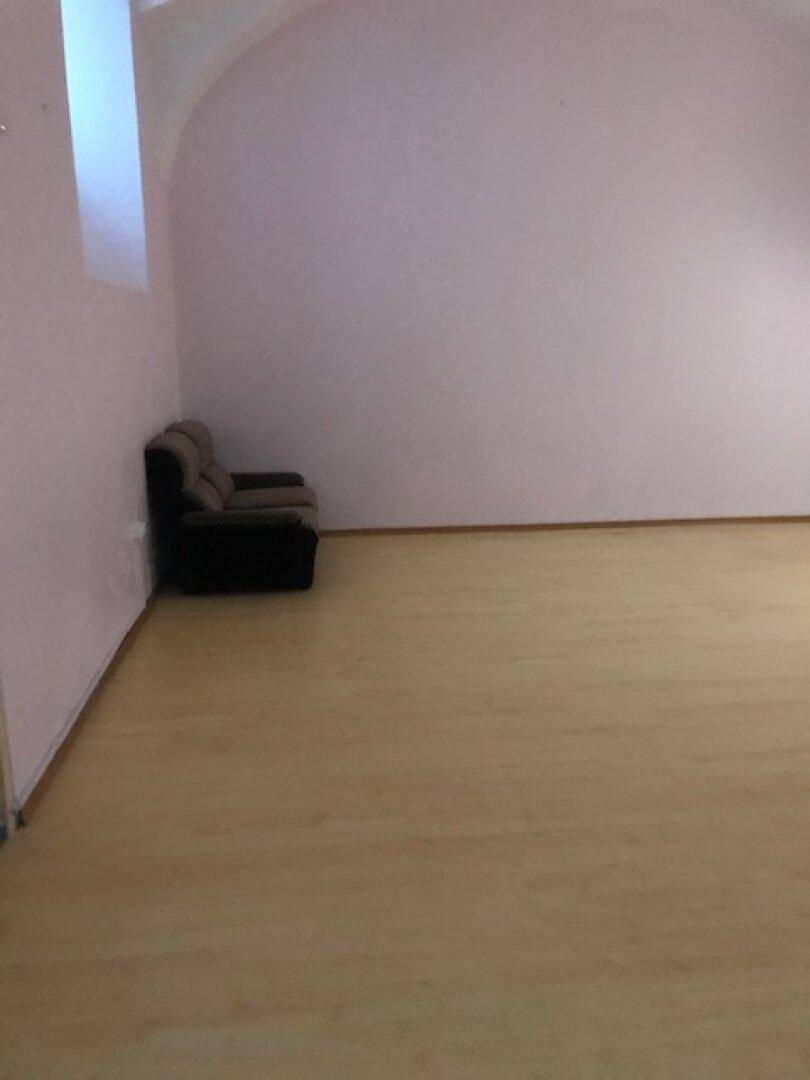 Leerer Raum mit hellvioletten Wänden, Laminatboden und einem kleinen Sofa in der Ecke.