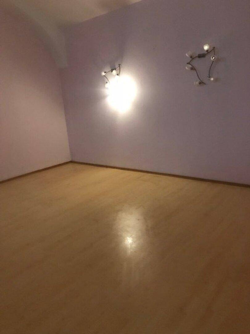Leerer Raum mit hellvioletten Wänden und hellem Laminatboden, beleuchtet von Wandlampen.