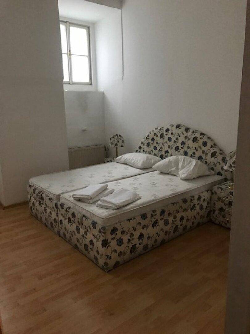 Schlafzimmer mit Bett, Fenster und hellem Laminatboden, das Bett hat ein florales Muster.