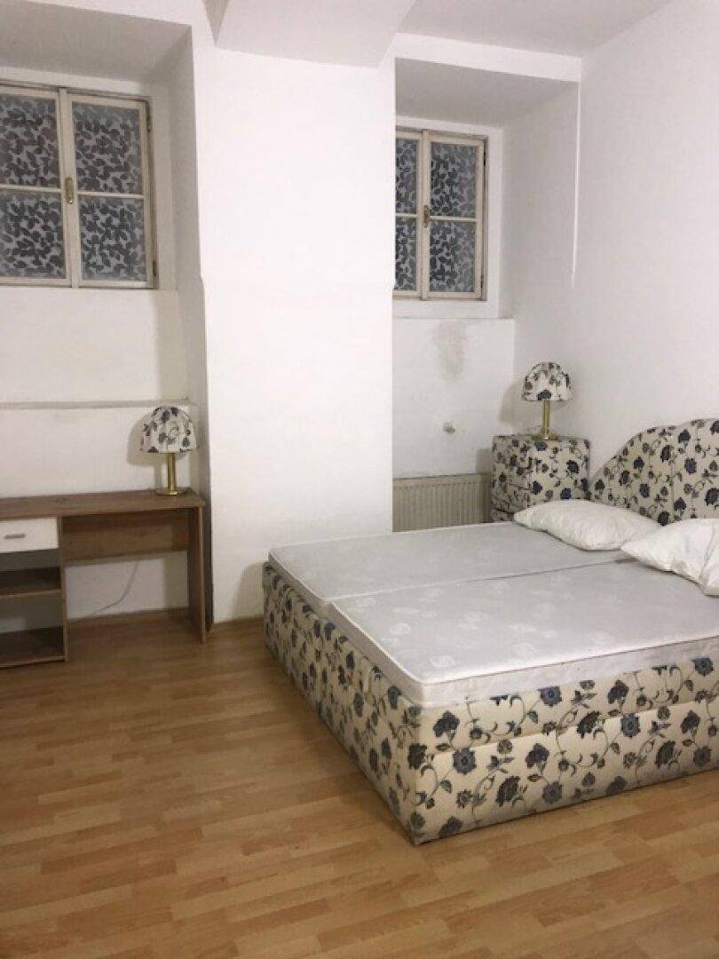 Schlafzimmer mit Bett, zwei Fenstern, Schreibtisch und hellem Laminatboden.