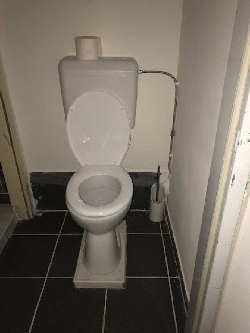 Separate Toilette mit WC und schwarzem Fliesenboden.