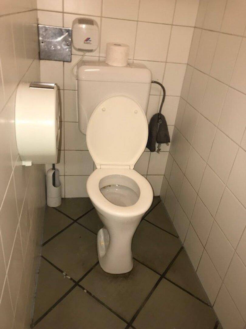 Separate Toilette mit WC und beigem Fliesenboden.