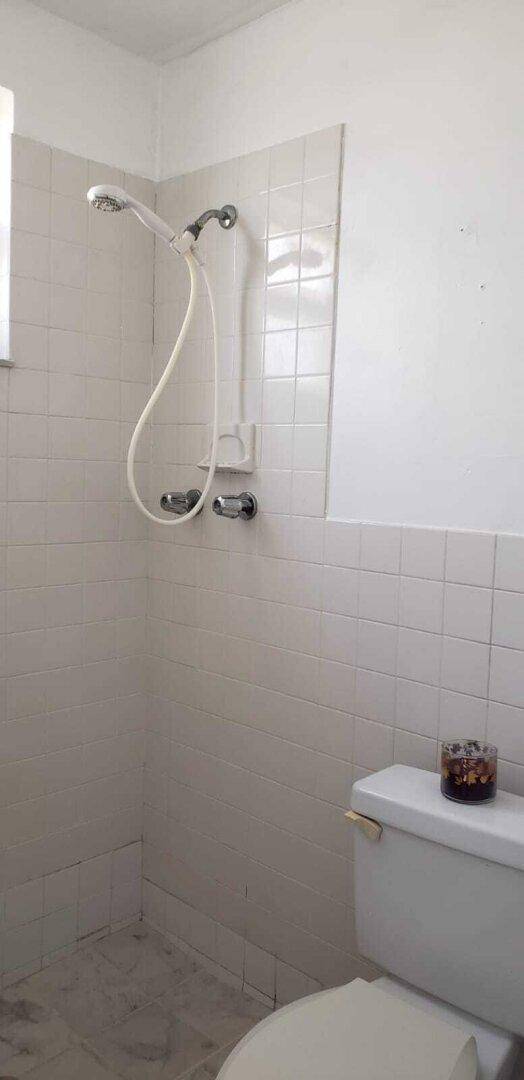 Badezimmer mit Dusche und Toilette, weißen Fliesen an den Wänden und hellem Fliesenboden.