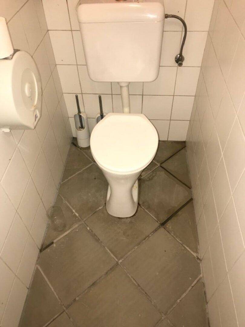 Separate Toilette mit WC und beigem Fliesenboden.