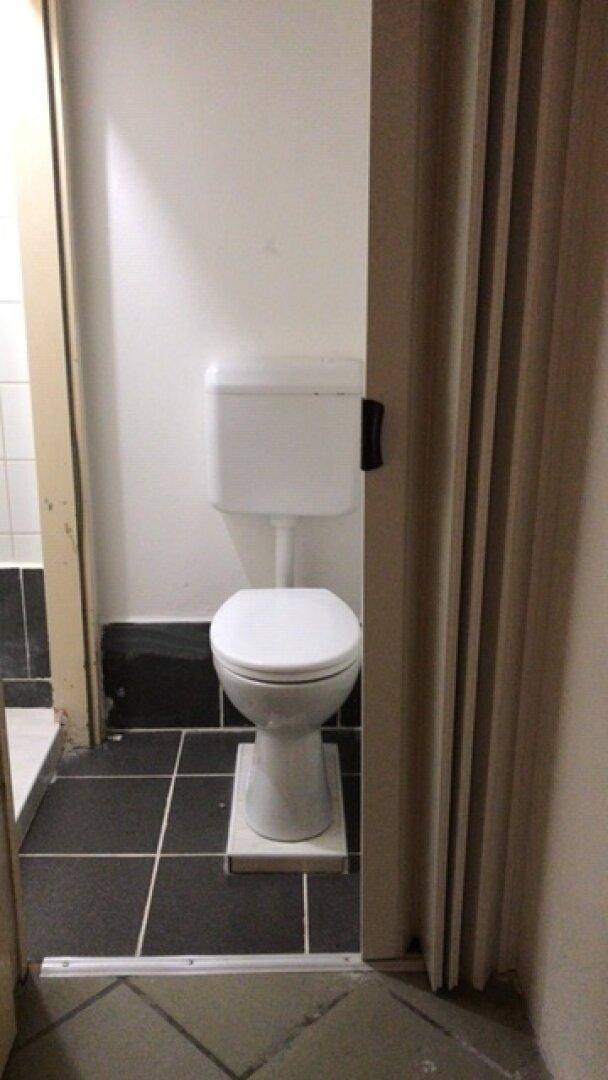 Separate Toilette mit WC und schwarzem Fliesenboden, teilweise verdeckt durch eine Falttür.