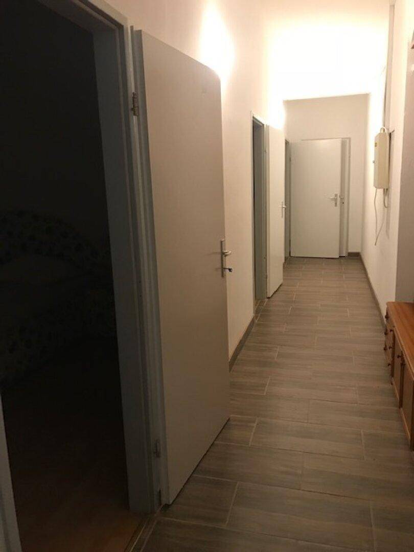 Langer Flur mit holzfarbenem Fliesenboden und mehreren Türen.