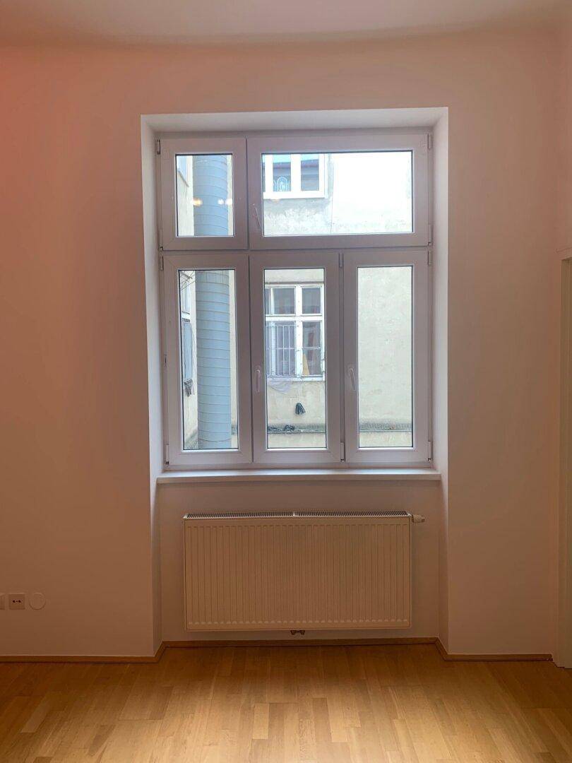 Heller Raum mit großem Fenster, Heizkörper und Parkettboden.
