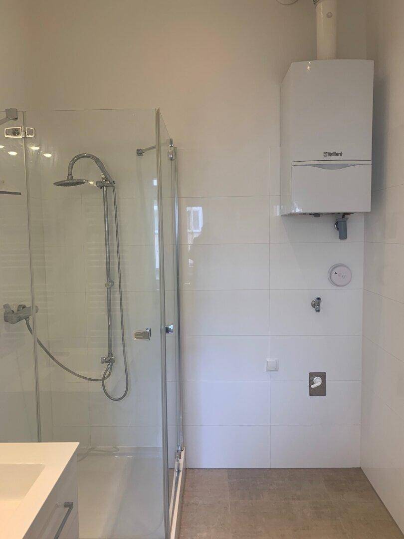 Duschbereich mit Glasabtrennung und wandmontiertem Warmwasserbereiter in modernem Bad.