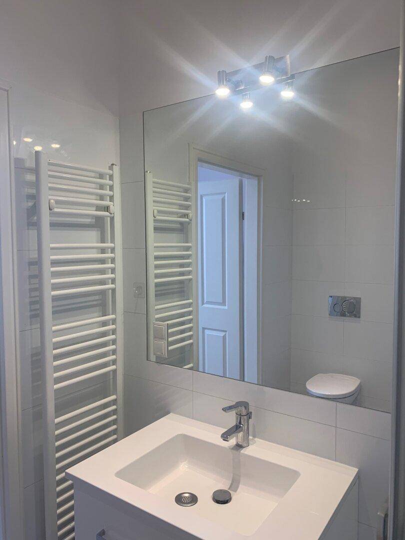 Modernes Badezimmer mit Waschbecken, großem Spiegel und beheiztem Handtuchhalter.