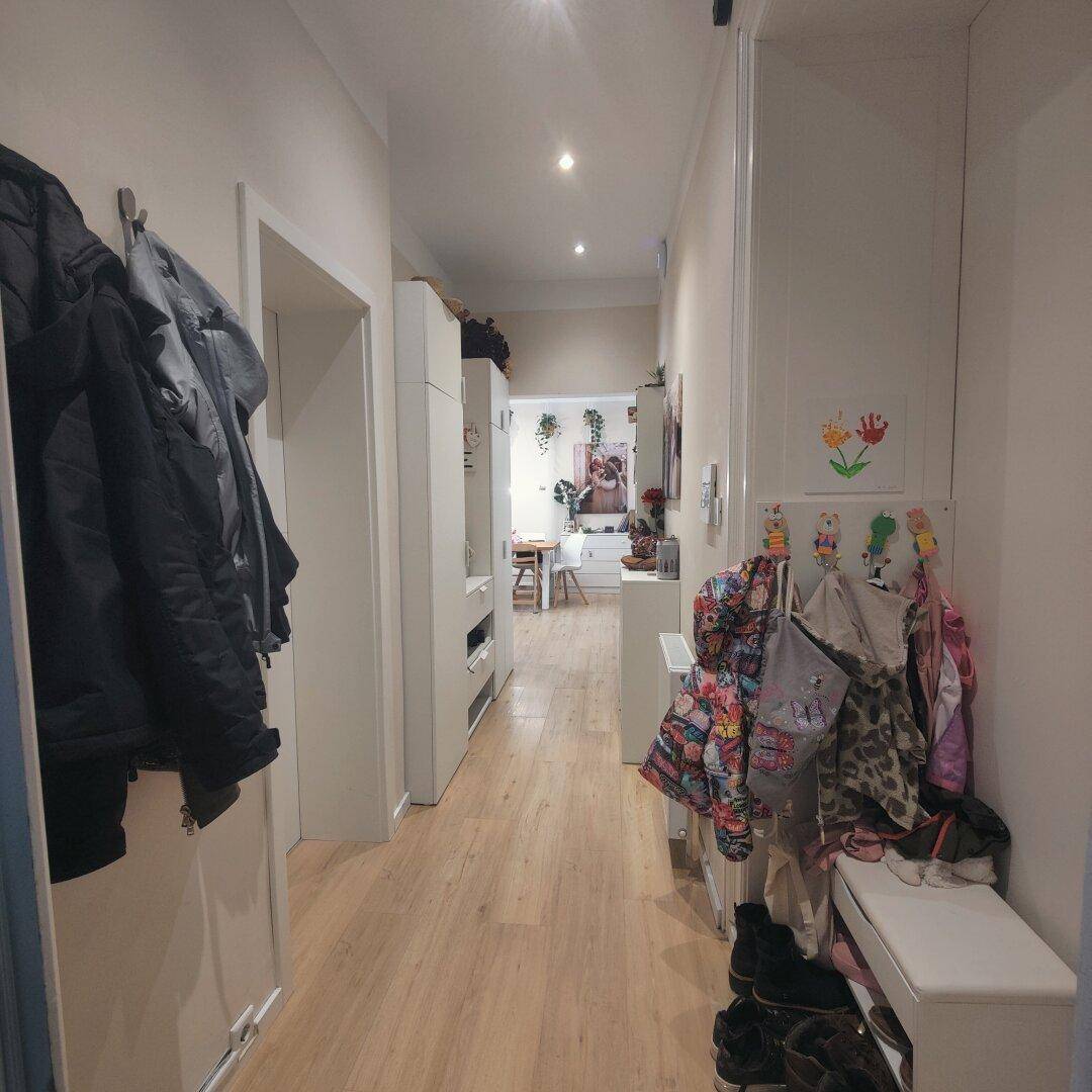 Heller Flur mit Holzfußboden, Garderobe und Kindersachen, der zu weiteren Räumen führt.