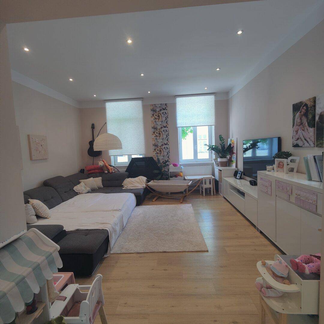 Geräumiges Wohnzimmer mit großem Sofa, Fernseher und Spielzeug, beleuchtet durch Einbaustrahler.