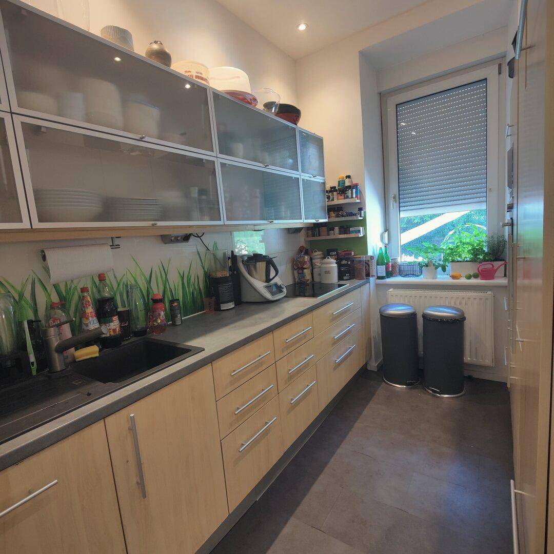 Moderne Küche mit hellen Holzschränken, dunkler Arbeitsplatte und einem Fenster mit Rollladen.