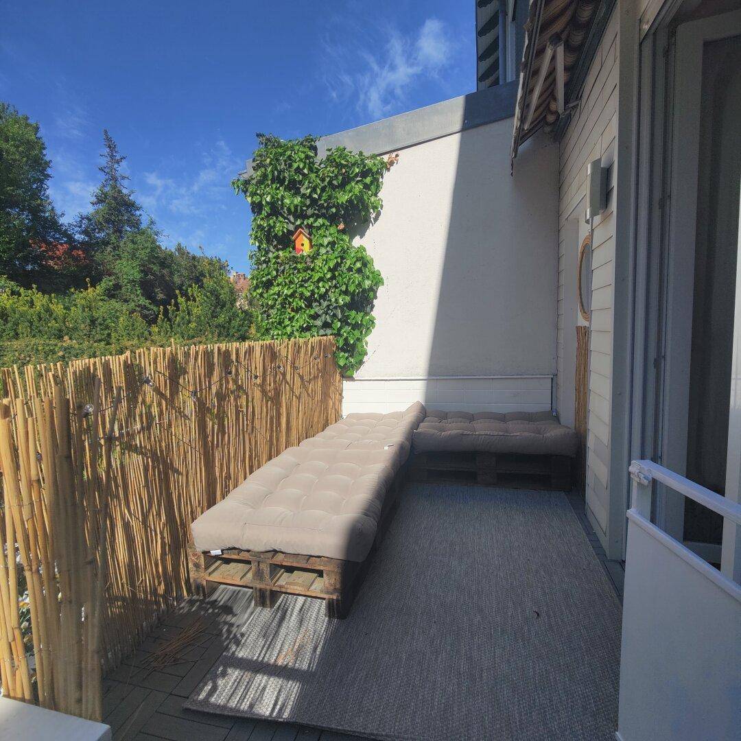 Sonniger Balkon mit bequemen Lounge-Möbeln und einem Sichtschutz aus Bambus für Privatsphäre.