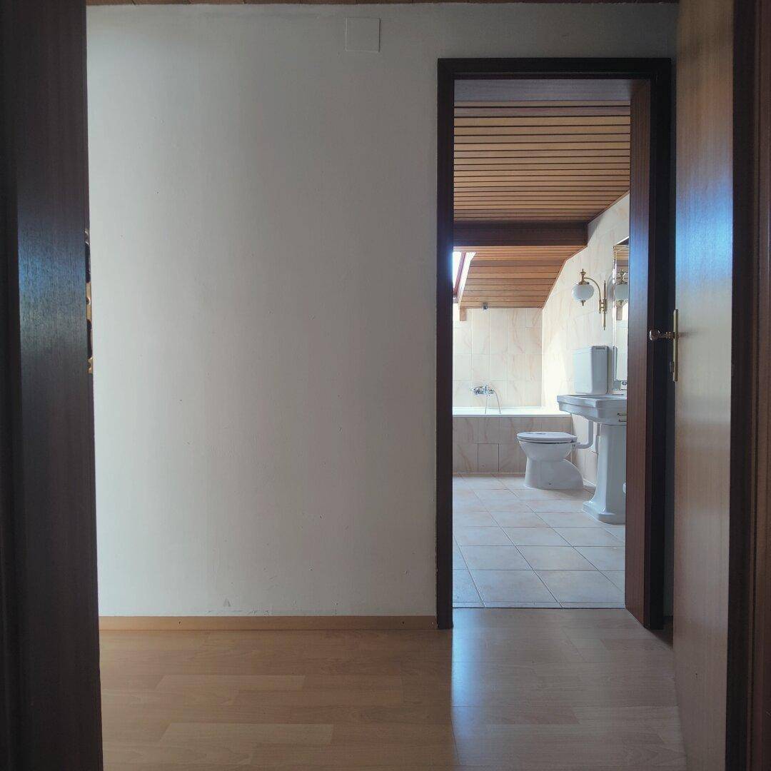 Blick in ein Badezimmer mit Badewanne, Waschbecken und Dachfenster, durch eine offene Tür.