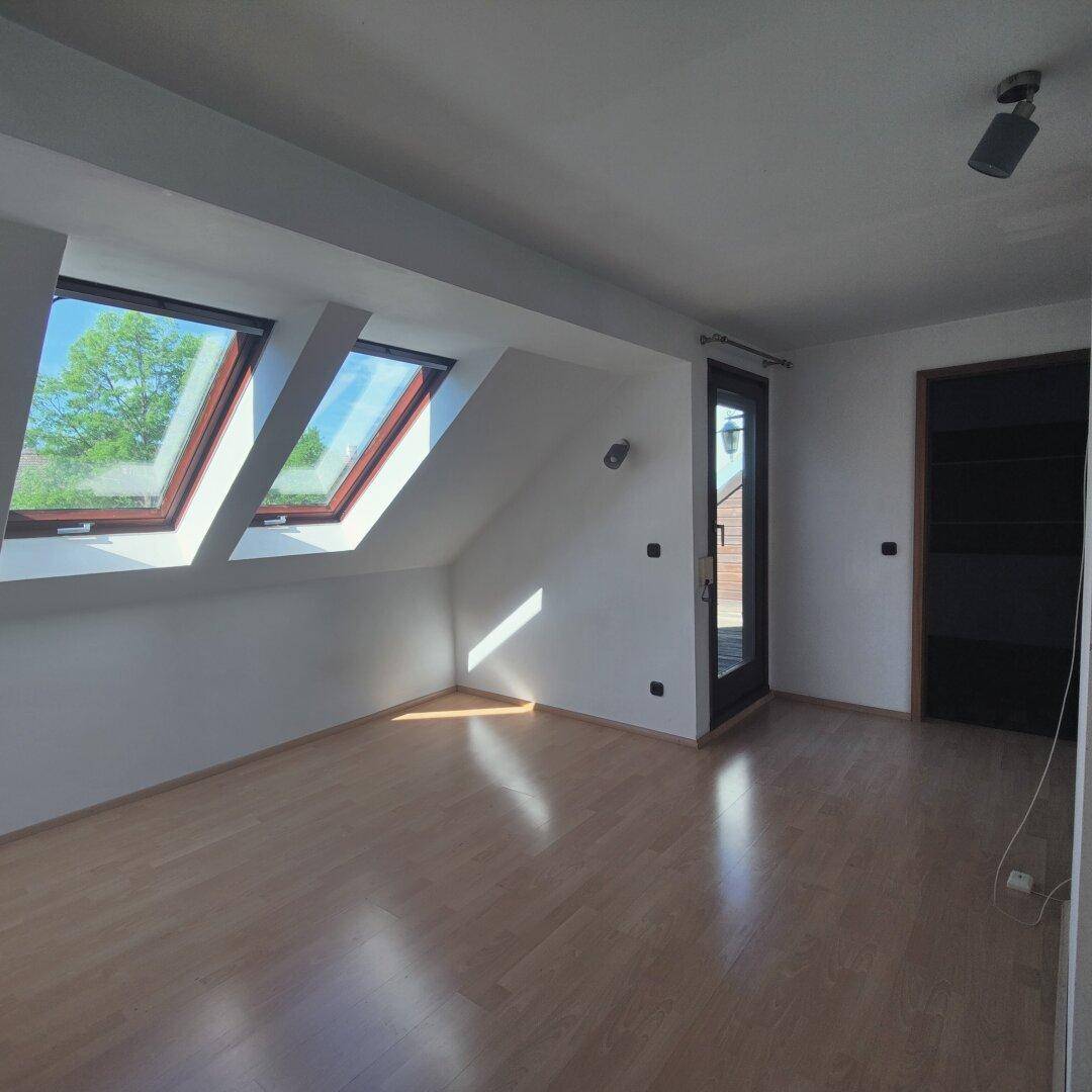Lichtdurchfluteter Dachgeschossraum mit Holzboden, Dachfenstern und Zugang zu einem Außenbereich.