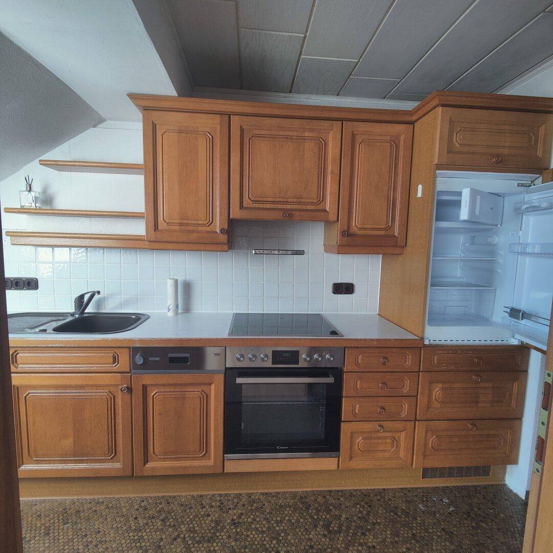 Traditionelle Küche mit Holzschränken, integriertem Kühlschrank und Kochfeld, unter einer Holzdecke.