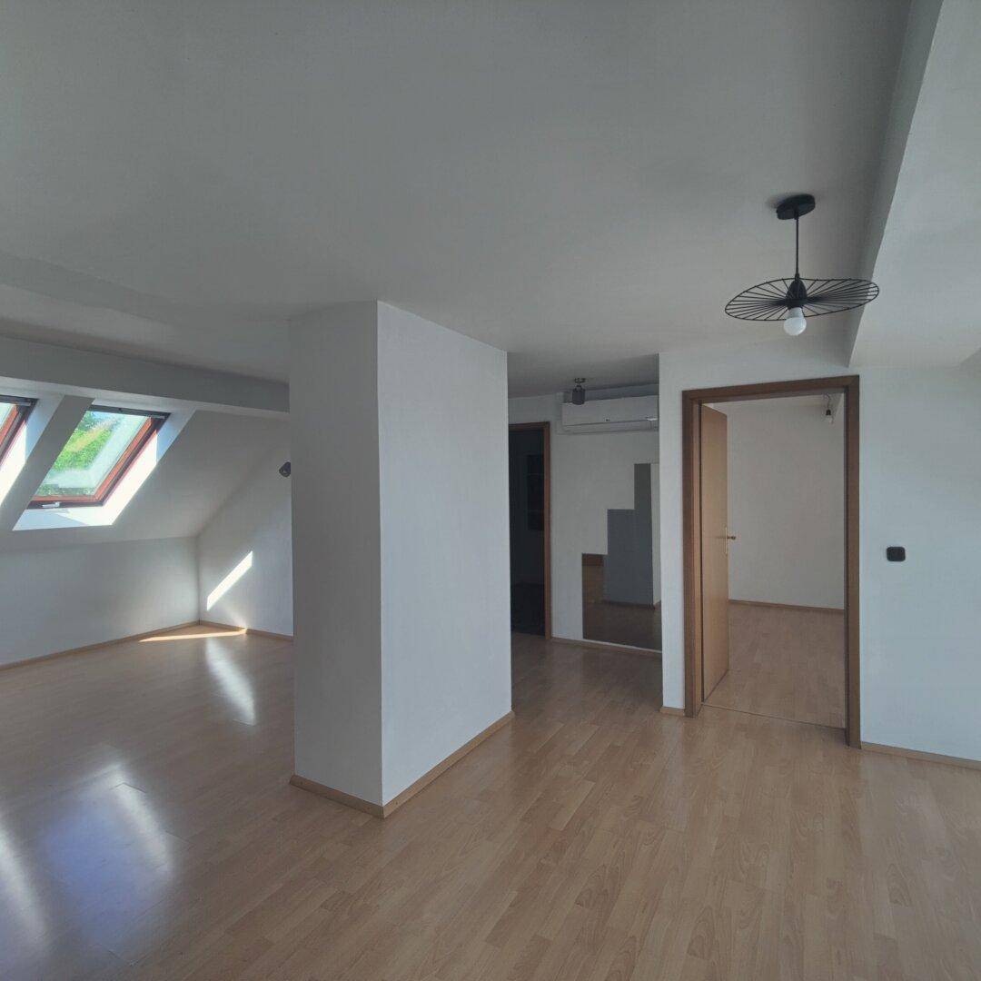 Heller und offener Dachgeschossraum mit Holzboden, schrägen Wänden und moderner Deckenleuchte.