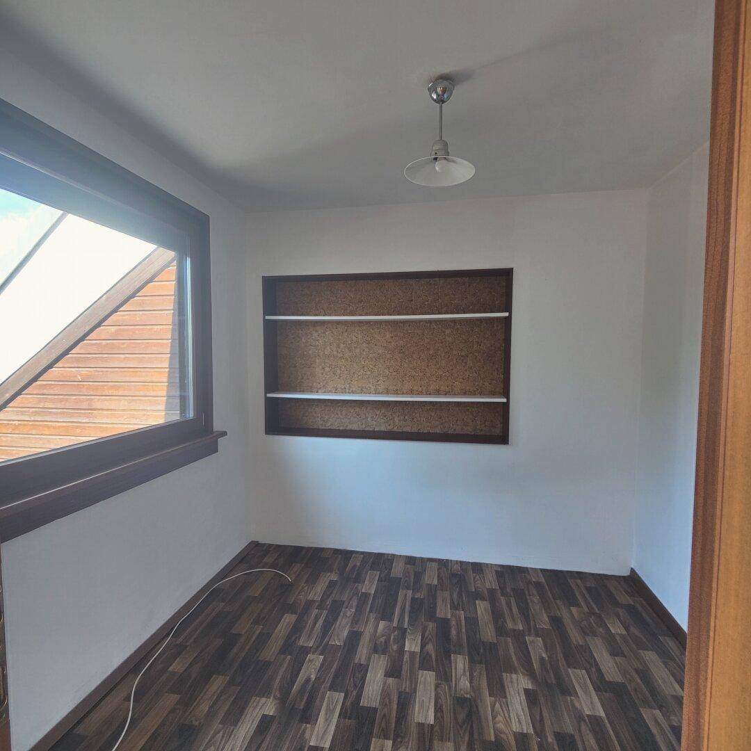 Kleiner Raum mit dunklem Holzboden, eingebauten Regalen und einem Fenster mit Blick nach draußen.