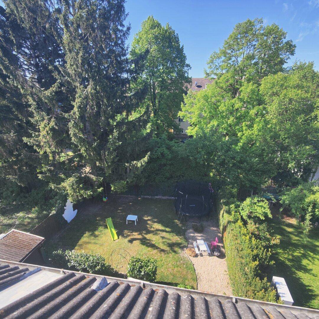 Blick von oben auf einen großen Garten mit Rasenfläche, Trampolin, Rutsche und hohen Bäumen.