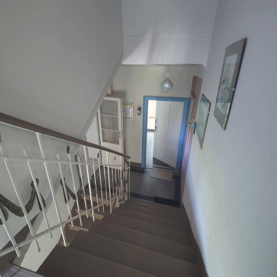 Treppenhaus mit Geländer und Fliesenboden, das zu weiteren Etagen und Wohnungen führt.