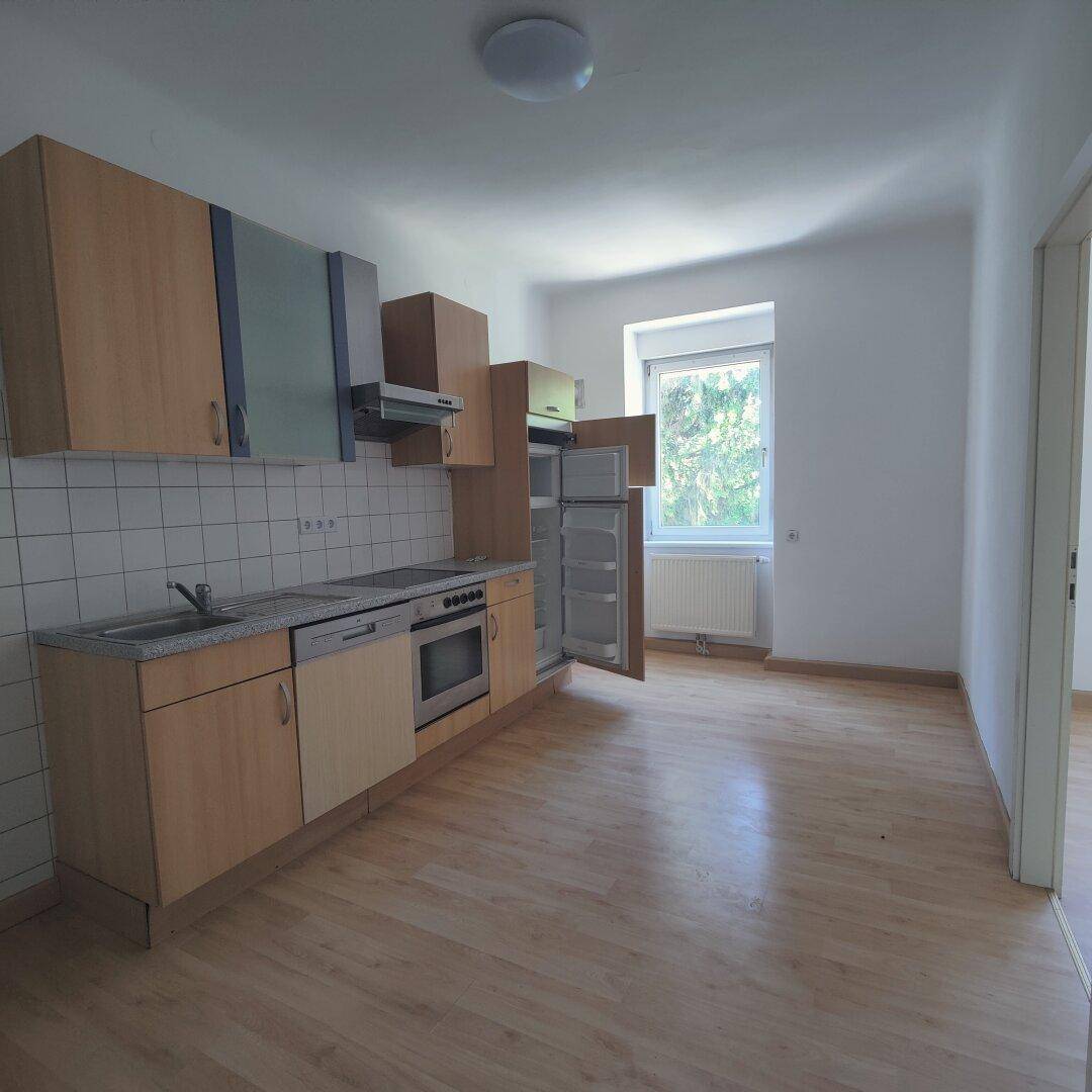 Einfache Küchenzeile in einem hellen Raum mit Holzfußboden und Fenster, inklusive Kühlschrank.