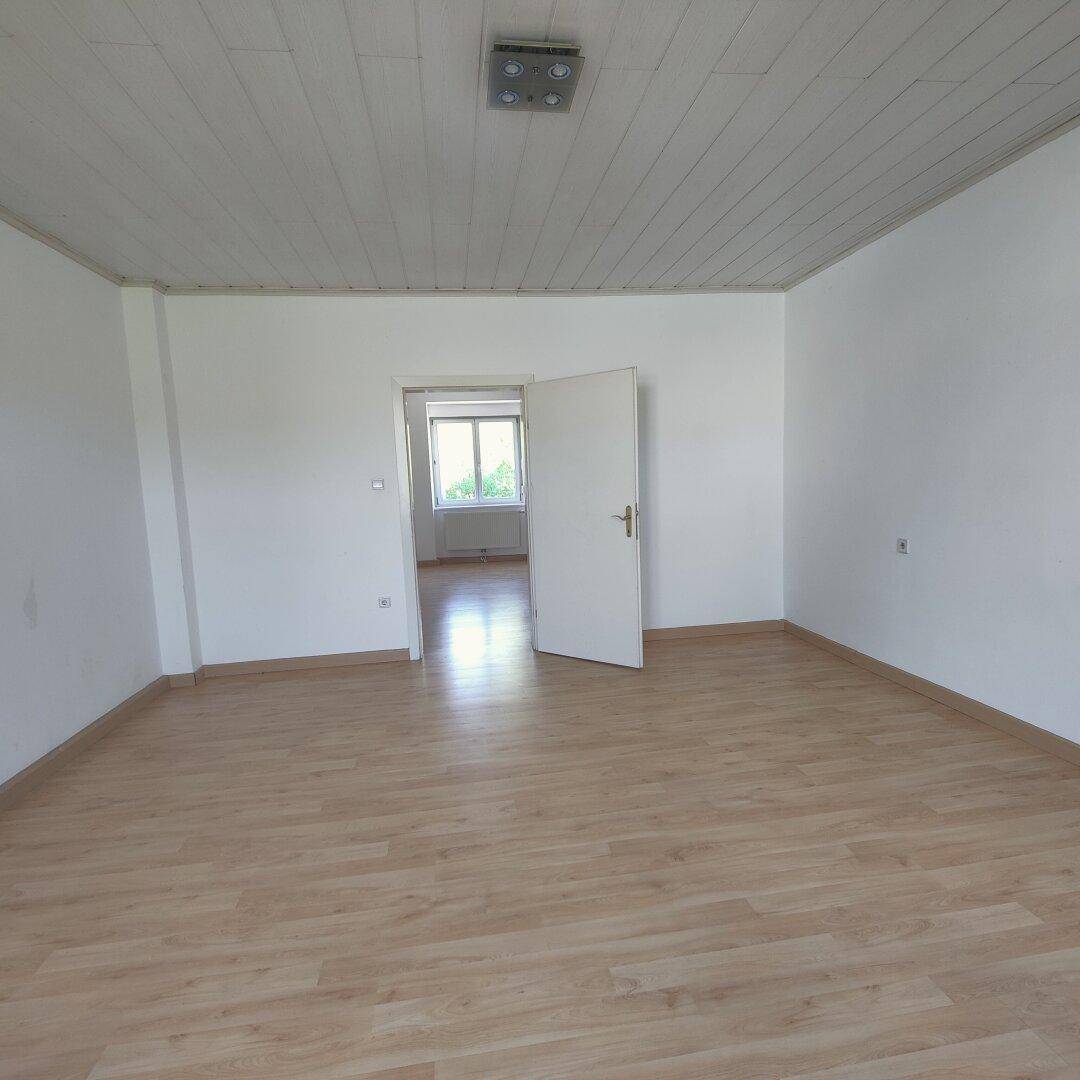 Geräumiger, heller Raum mit Holzfußboden und weißer Deckenverkleidung, ideal für Wohnzwecke.