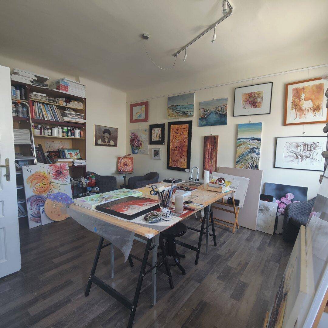 Kreatives Atelier mit großem Arbeitstisch, zahlreichen Kunstwerken und Bücherregalen, ideal für Künstler.