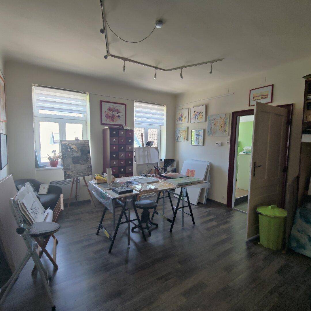 Helles Atelier mit zwei Fenstern, gefüllt mit Kunstwerken und Malutensilien, bietet viel Tageslicht.