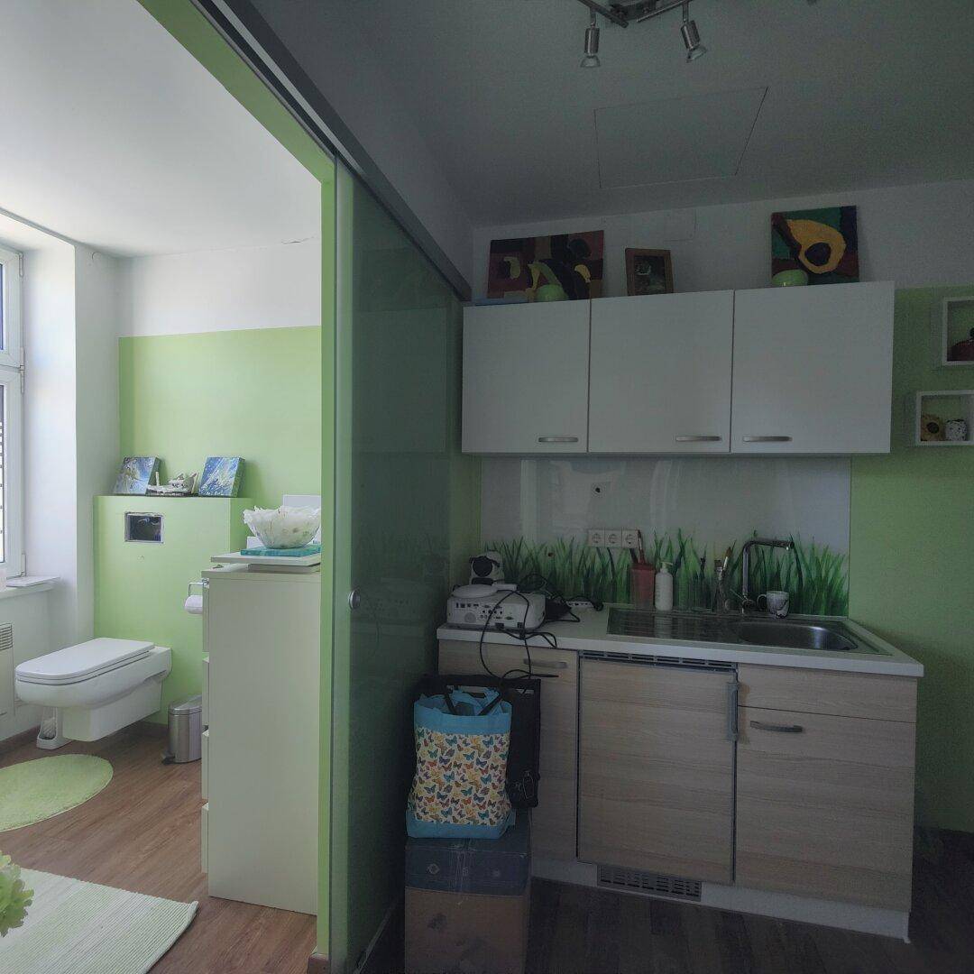 Kompakte Küchenzeile mit Spüle und Oberschränken, angrenzend an ein Badezimmer mit Schiebetür.