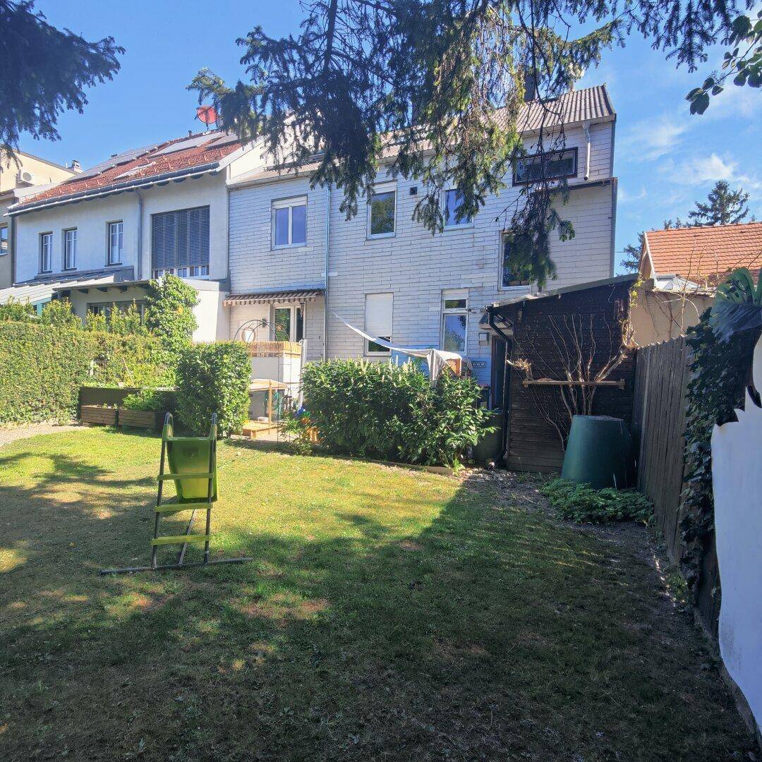 Großer Garten mit Rasenfläche, Hecken und der Rückseite des Gebäudes, bietet viel Platz im Freien.