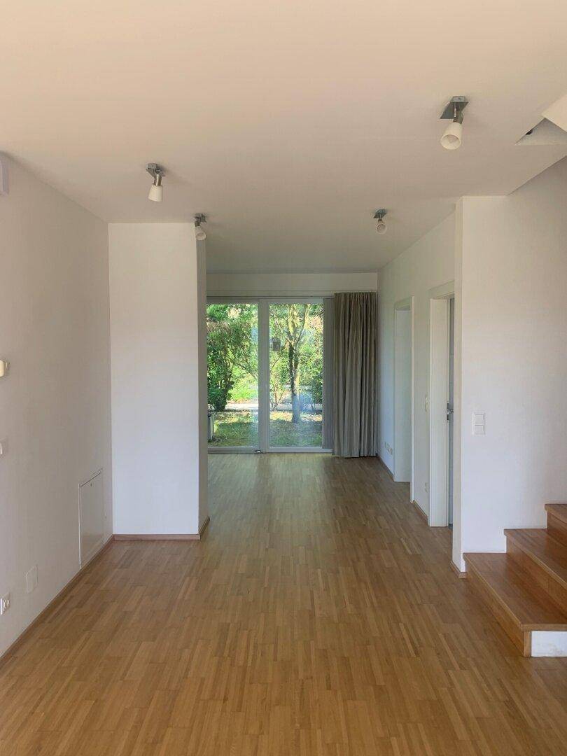 Heller Wohnbereich mit Holzboden und großen Fenstern, die viel Tageslicht hereinlassen.