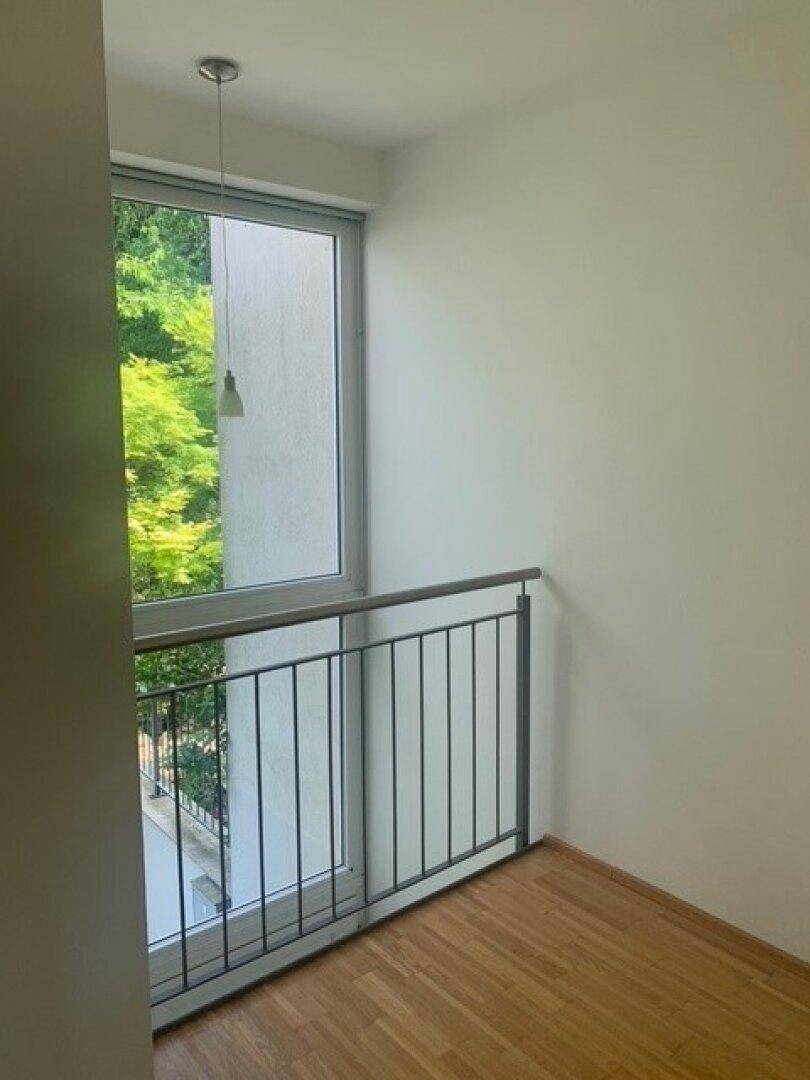 Heller Flurbereich mit Fenster und Geländer, das einen Blick ins Grüne bietet.
