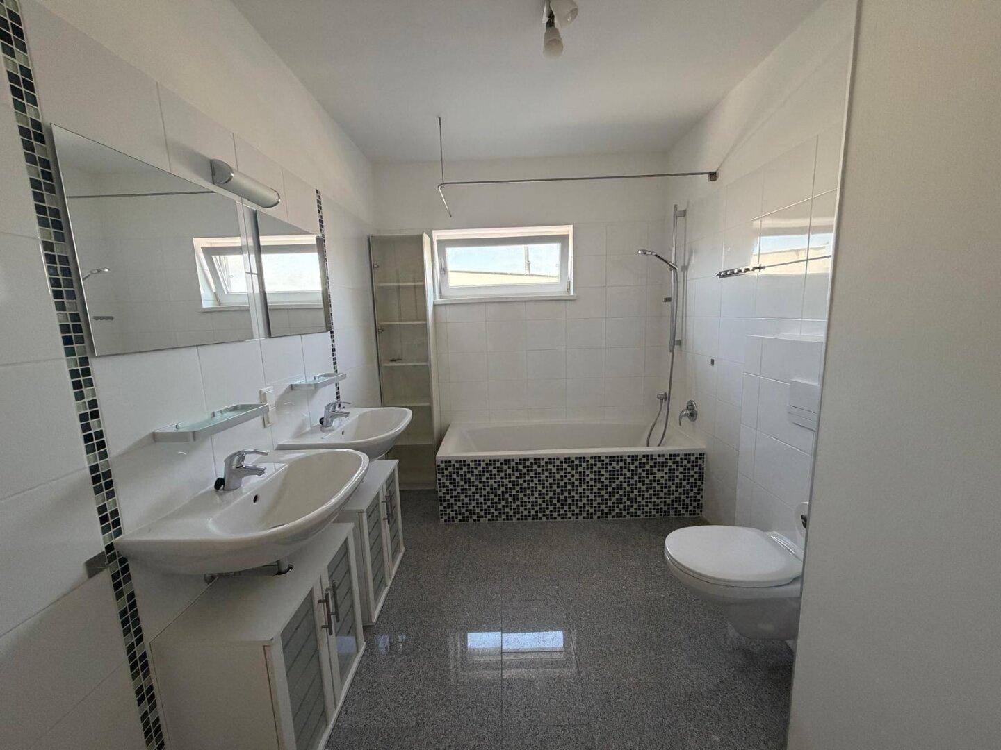 Modernes Badezimmer mit Doppelwaschbecken, Badewanne und Fenster für natürliches Licht.