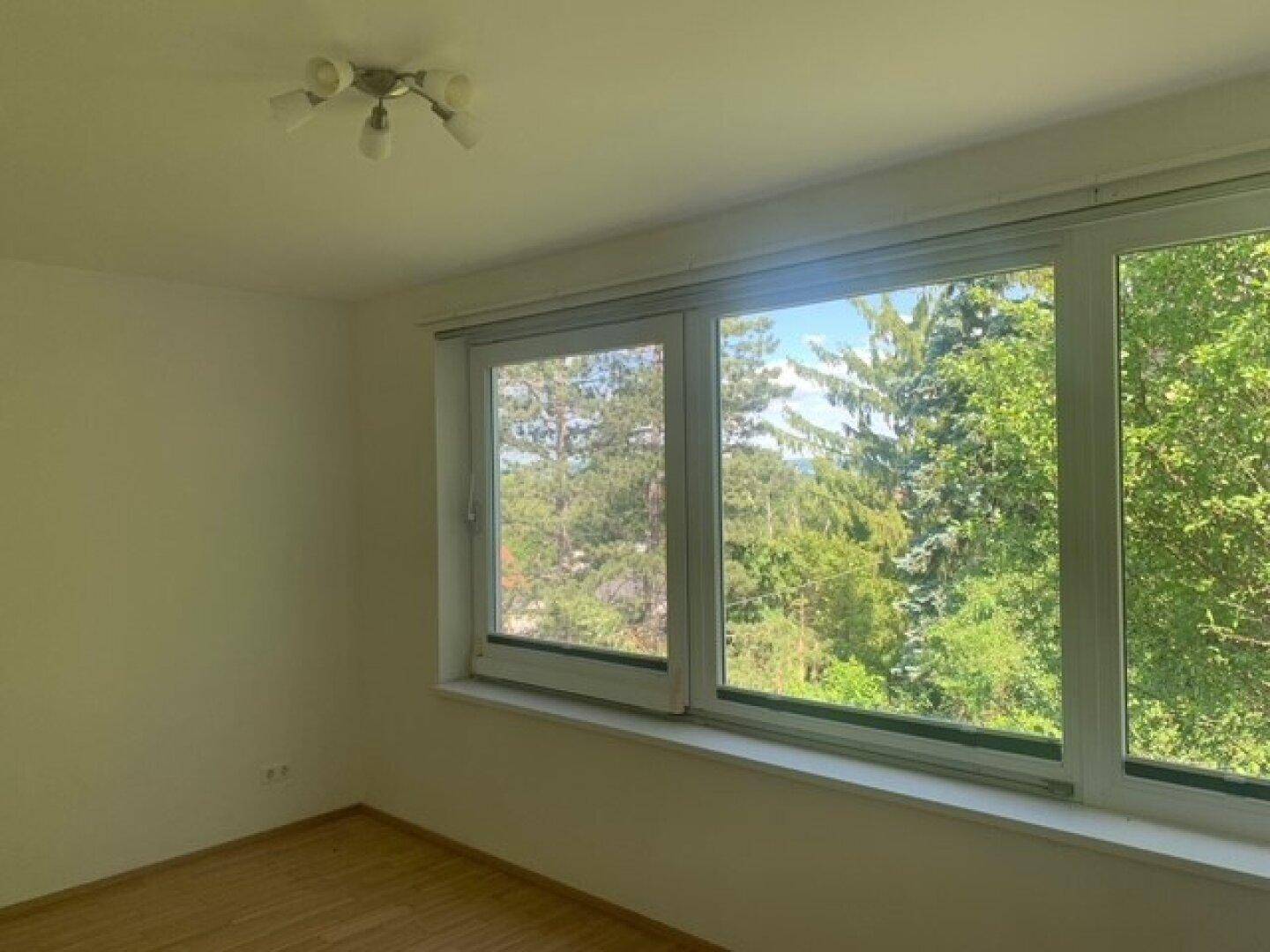 Helles Schlafzimmer mit großem Fenster und beruhigendem Blick auf die umliegenden Bäume.