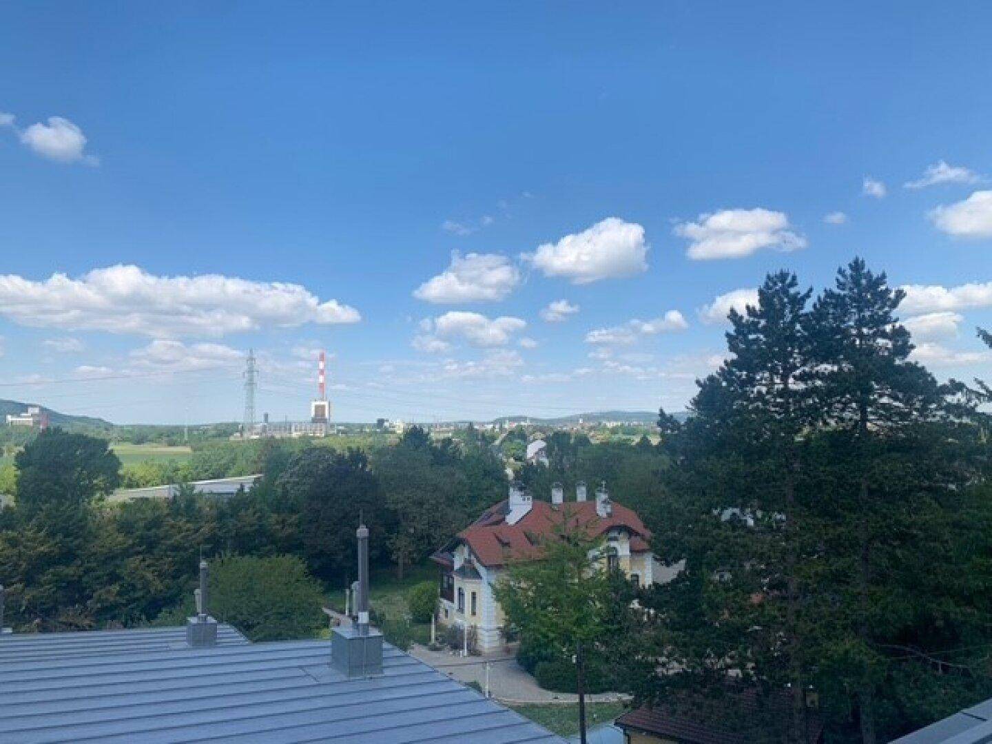 Panoramablick über eine grüne Landschaft mit Wohngebäuden und einem markanten Schornstein in der Ferne.